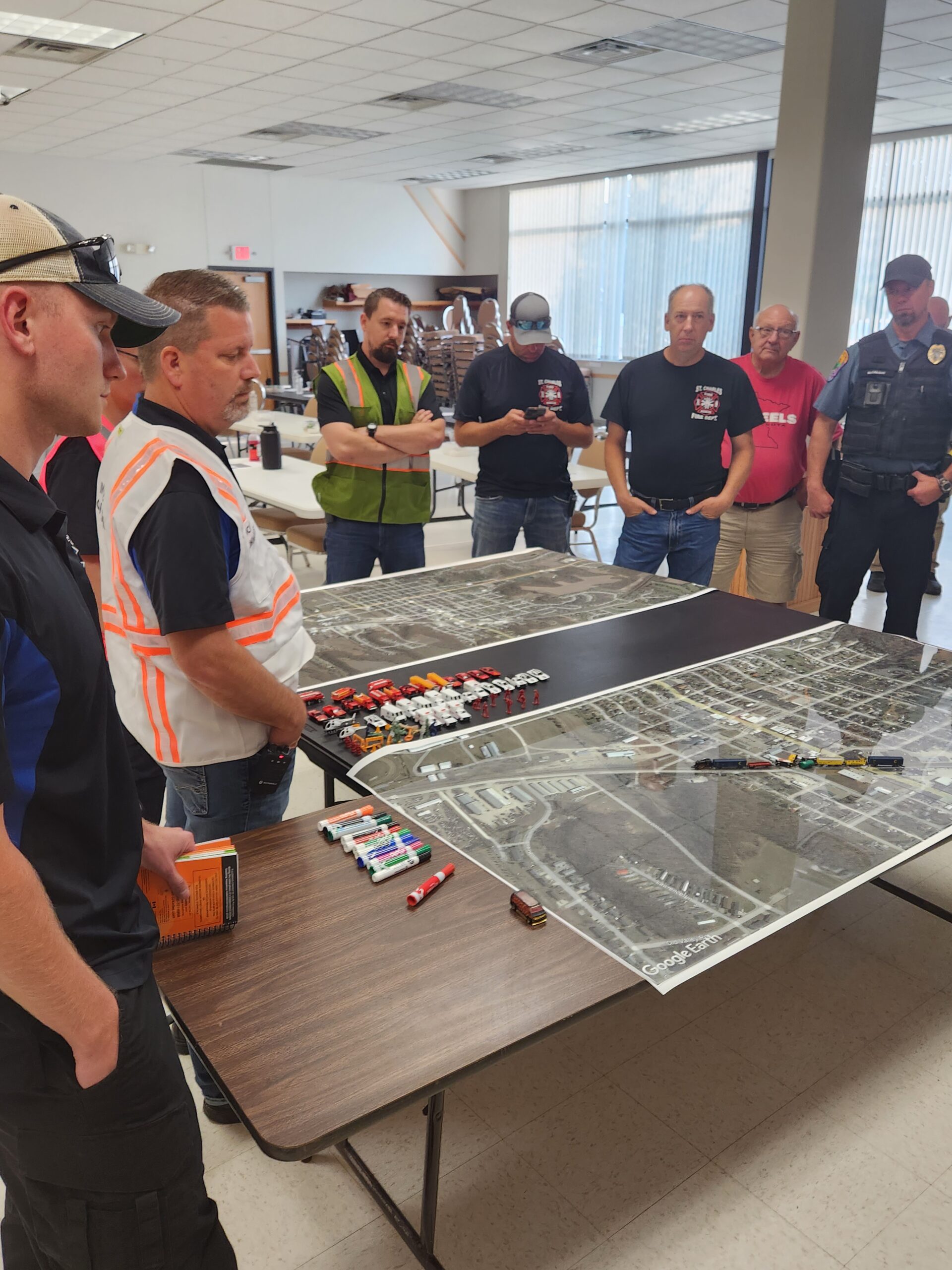 Planning meeting with men gathered around a table with a map and small objects used to visualize something.